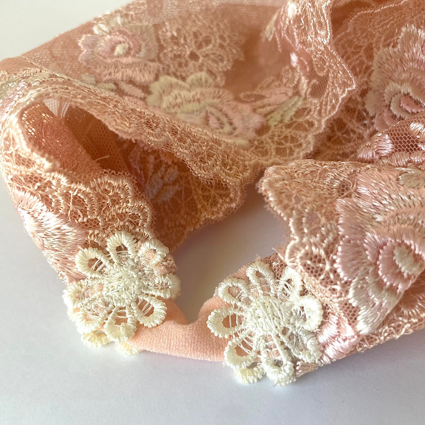 Peach-colored lace baby veil with rose embroidery. The veil headband features a stretchy elastic nylon and floral embroidery.