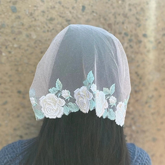 Woman wearing a pink lace chapel veil with white rose embroidery. The Traditional Catholic Christian Mass mantilla is tied on