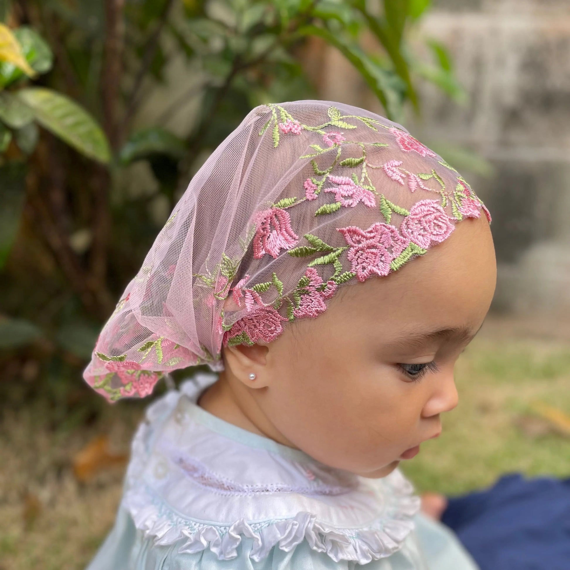 Baby wearing a soft pink embroidered lace chapel veil, perfect for attending Catholic Mass. 