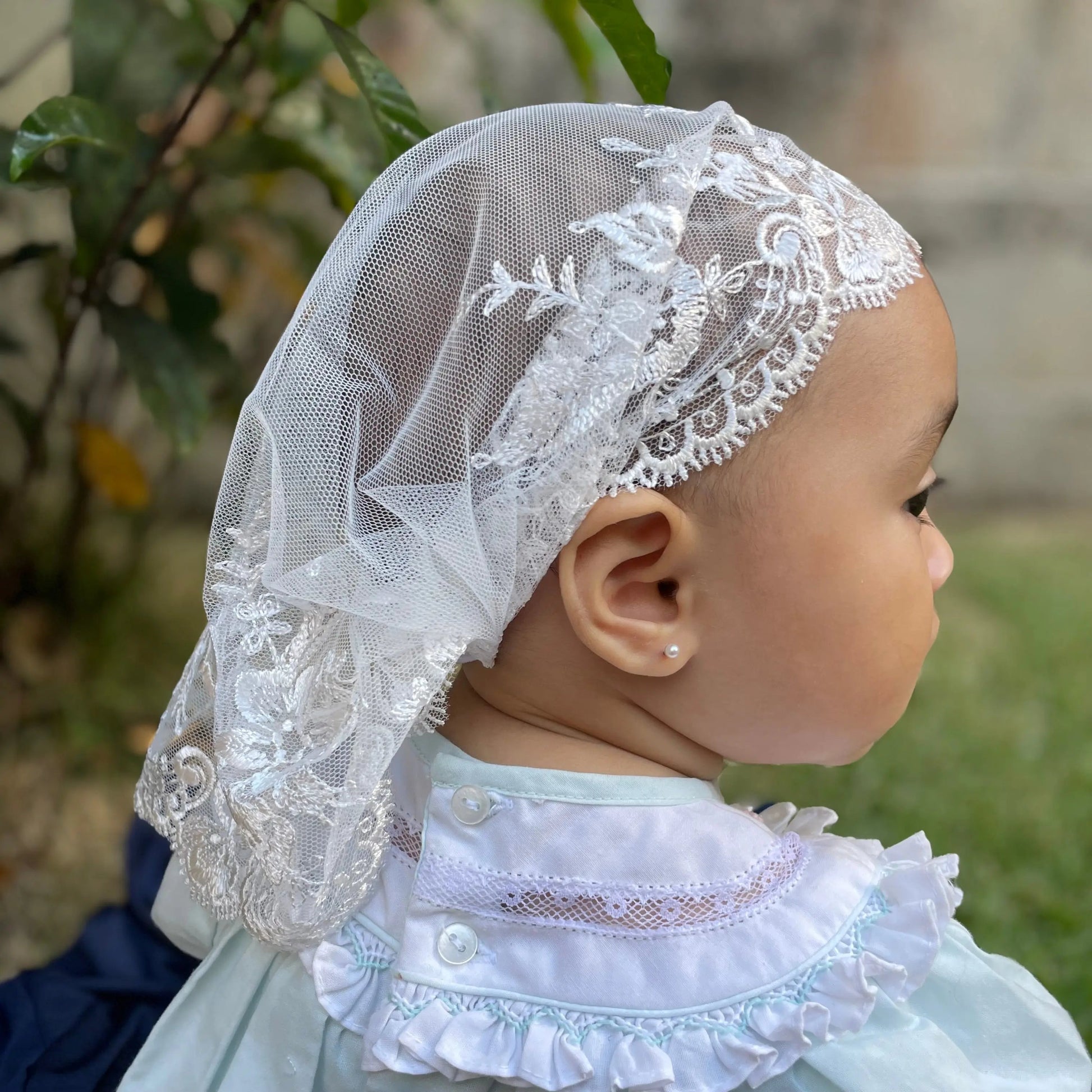 Infant wearing an ivory embroidered lace chapel veil for Traditional Catholic Mass.