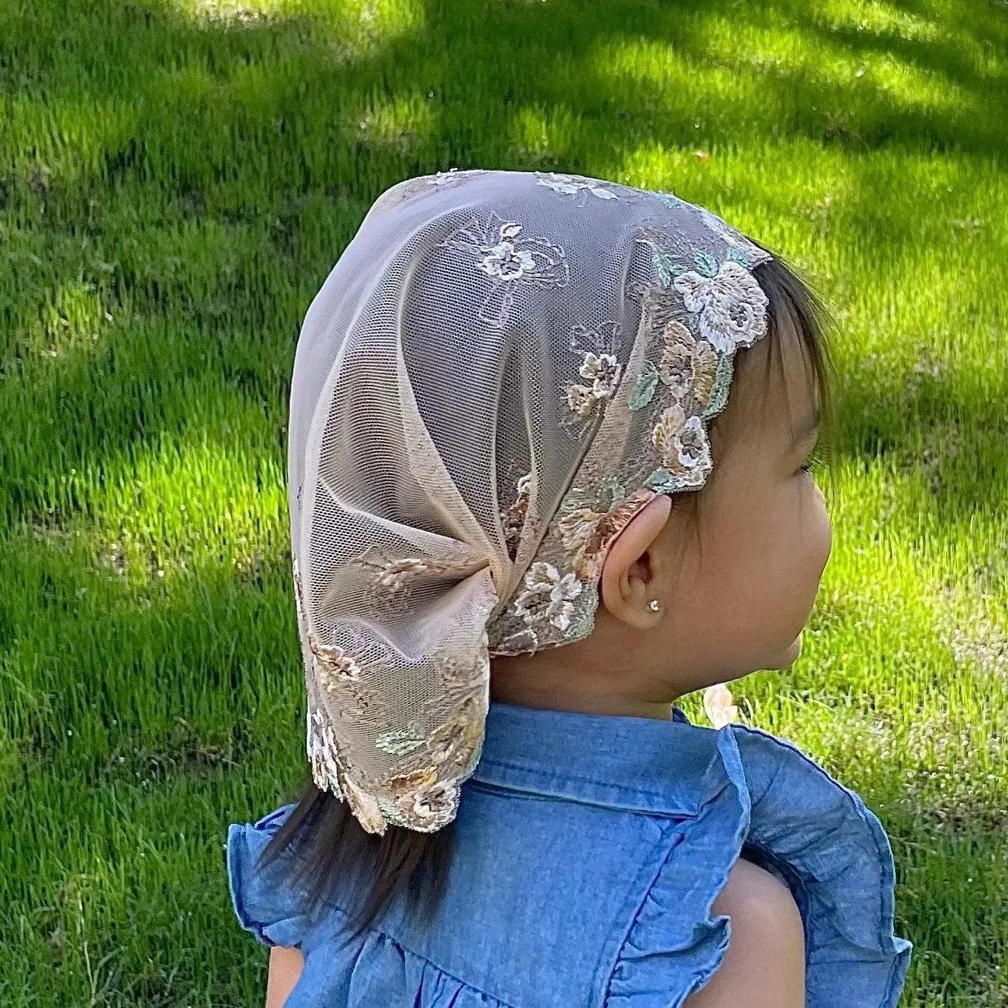 Baby wearing a traditional beige embroidered chapel veil for Catholic prayer.