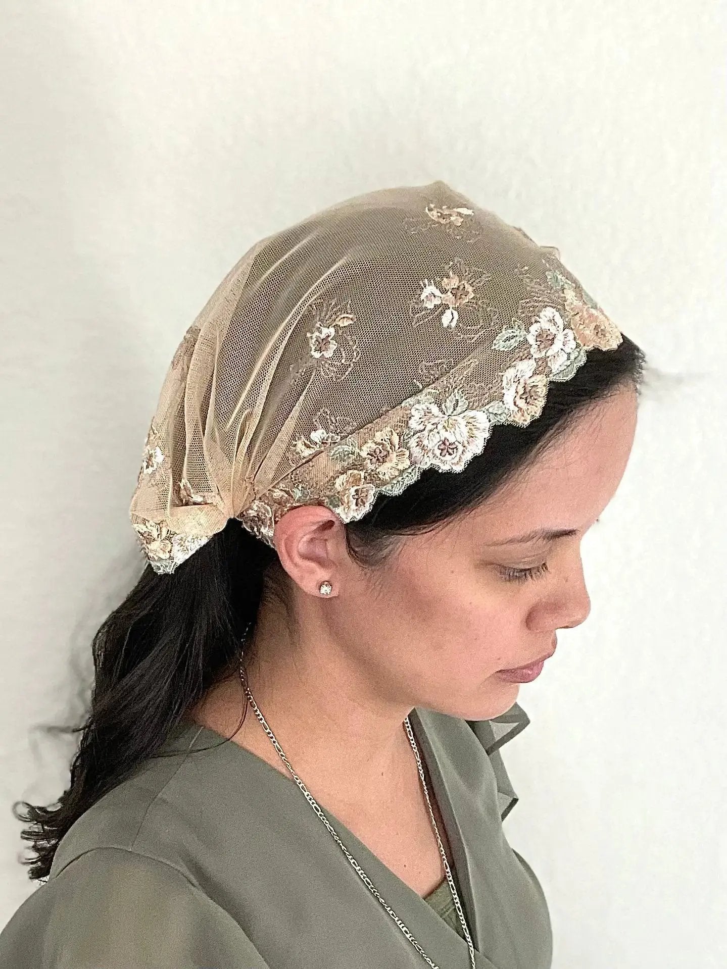 Girl wearing a beige lace embroidered traditional Catholic mass veil bandana.