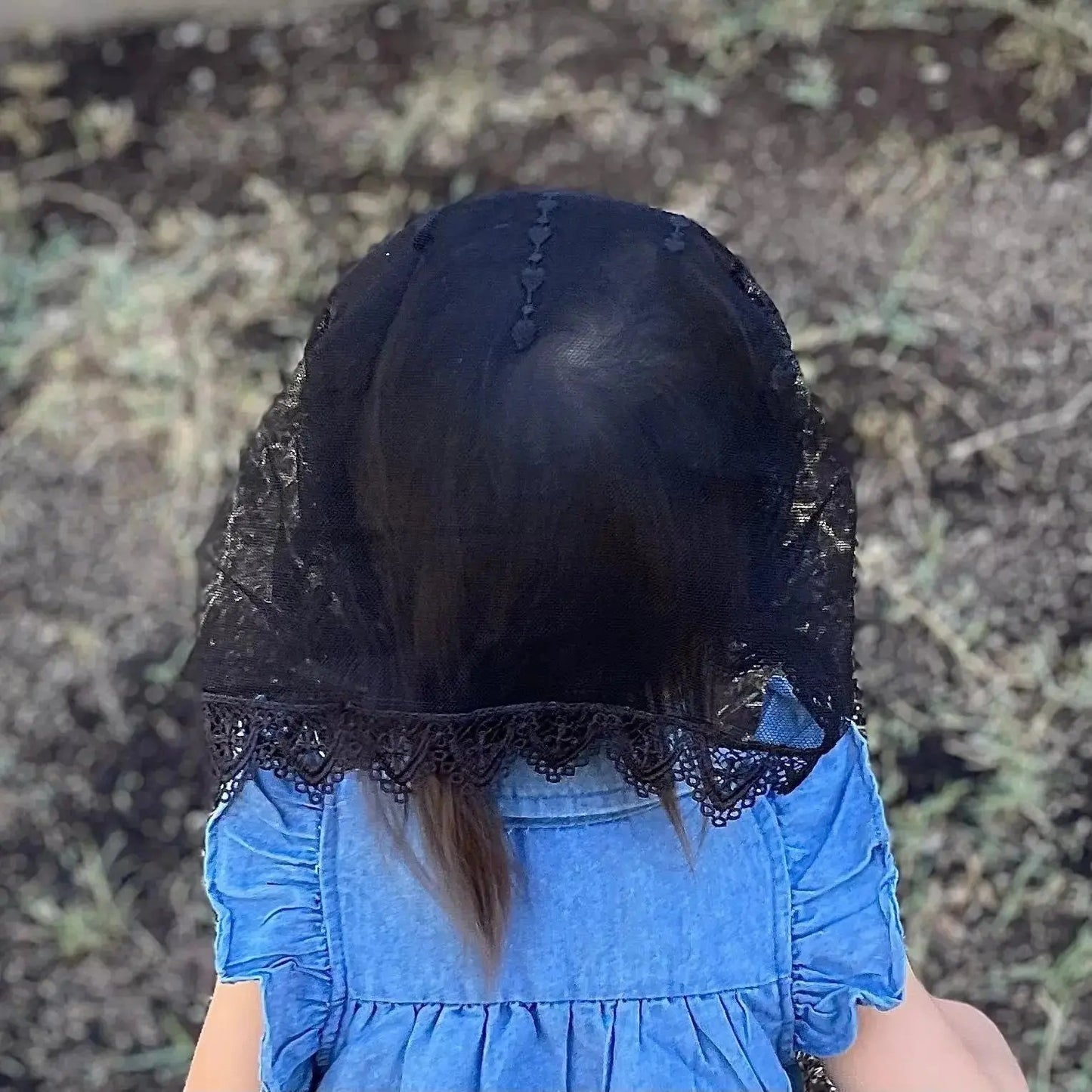 Back view of a toddler wearing a black colored lace chapel veil for Catholic Mass.