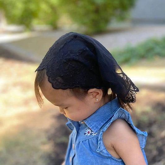 Baby wearing a traditional christian embroidered lace chapel veil for mass.