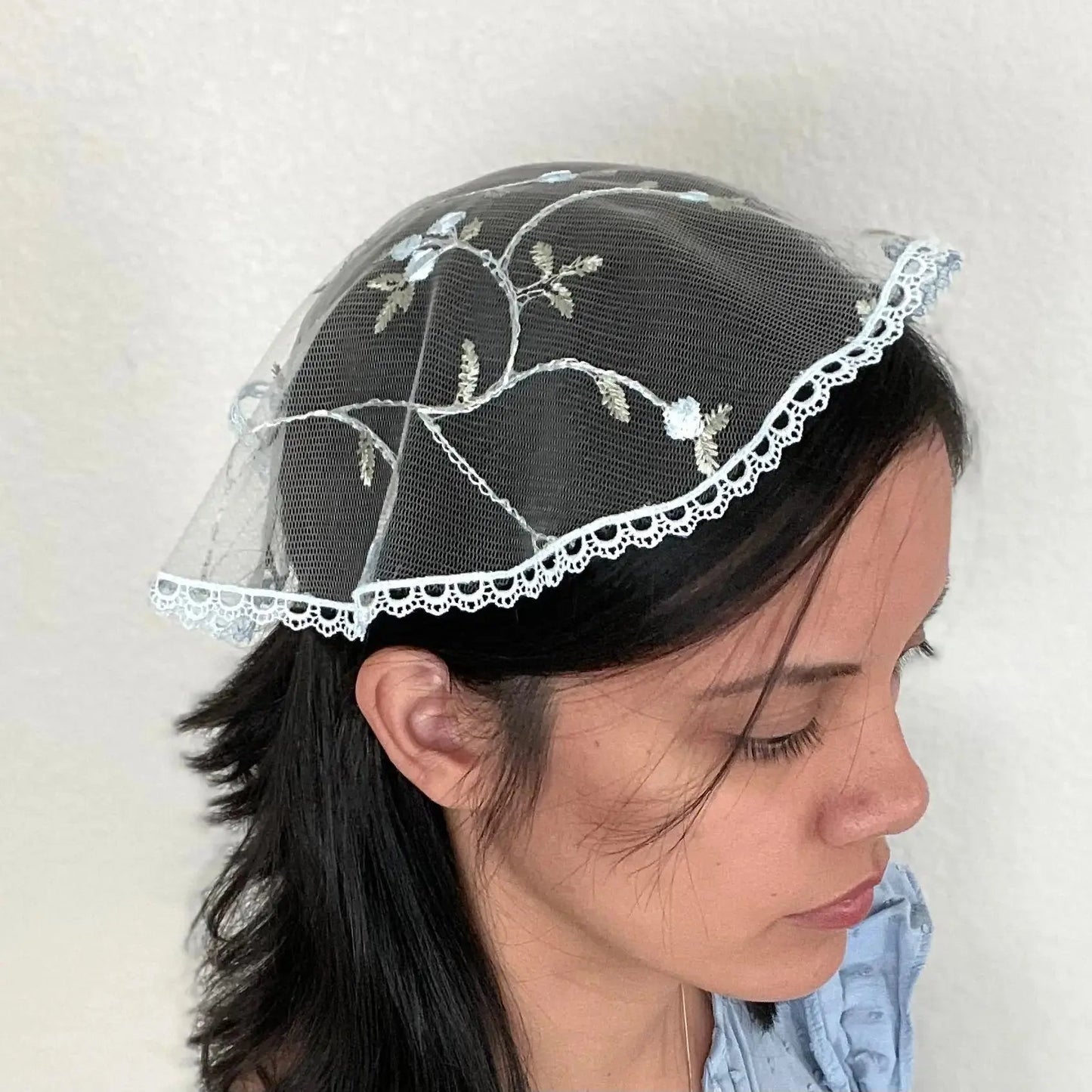 Girl wearing a blue floral embroidered lace cap chapel veil for Catholic mass.
