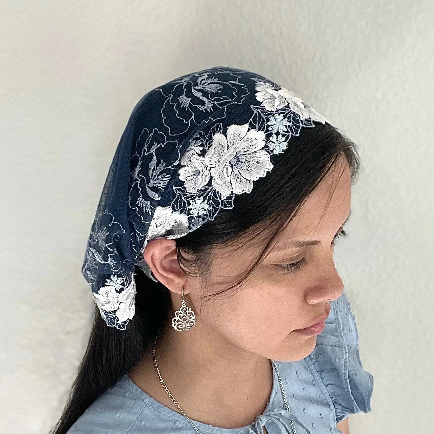 Woman wearing a blue lace chapel veil with rose embroidery. The small Traditional Catholic Christian Mass mantilla has ties