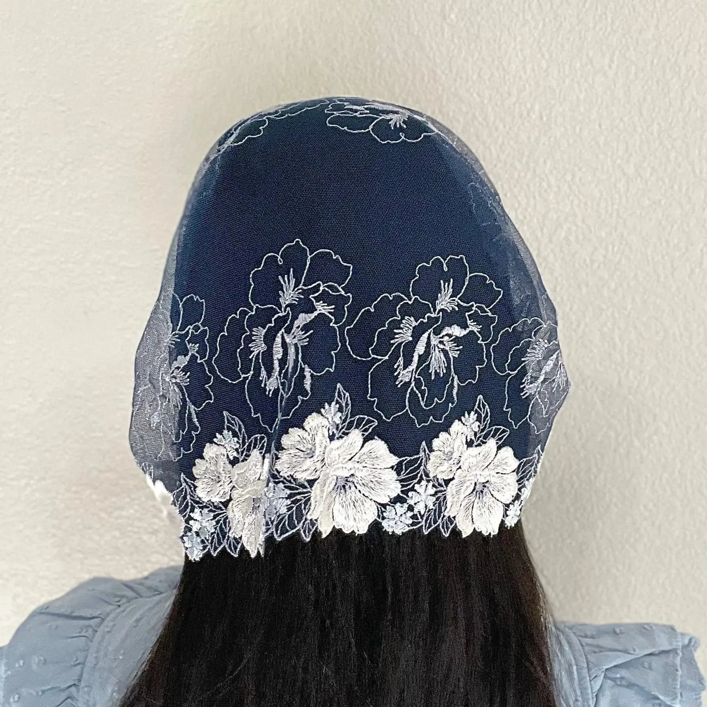Woman wearing a dark blue lace chapel veil with white rose embroidery. The small Traditional Catholic Christian Mass mantilla