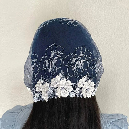 Woman wearing a dark blue lace chapel veil with white rose embroidery. The small Traditional Catholic Christian Mass mantilla