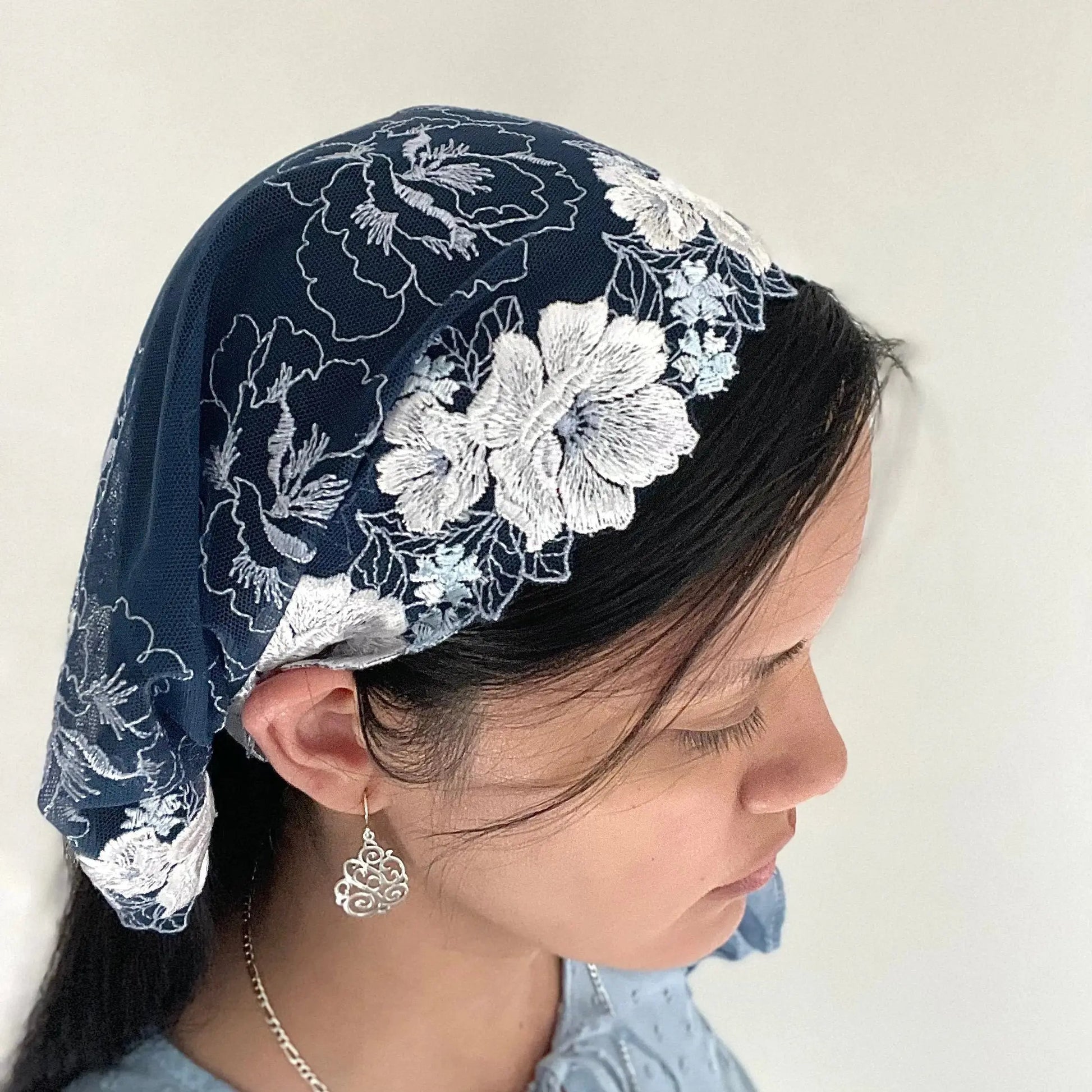 Girl wearing a dark blue chapel veil with rose embroidery. The small Traditional Catholic Christian Mass mantilla is tied on.