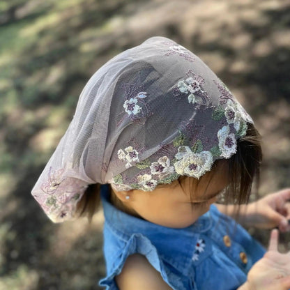 An infant wearing delicate purple embroidered lace Catholic chapel veil, a traditional mass veil. 