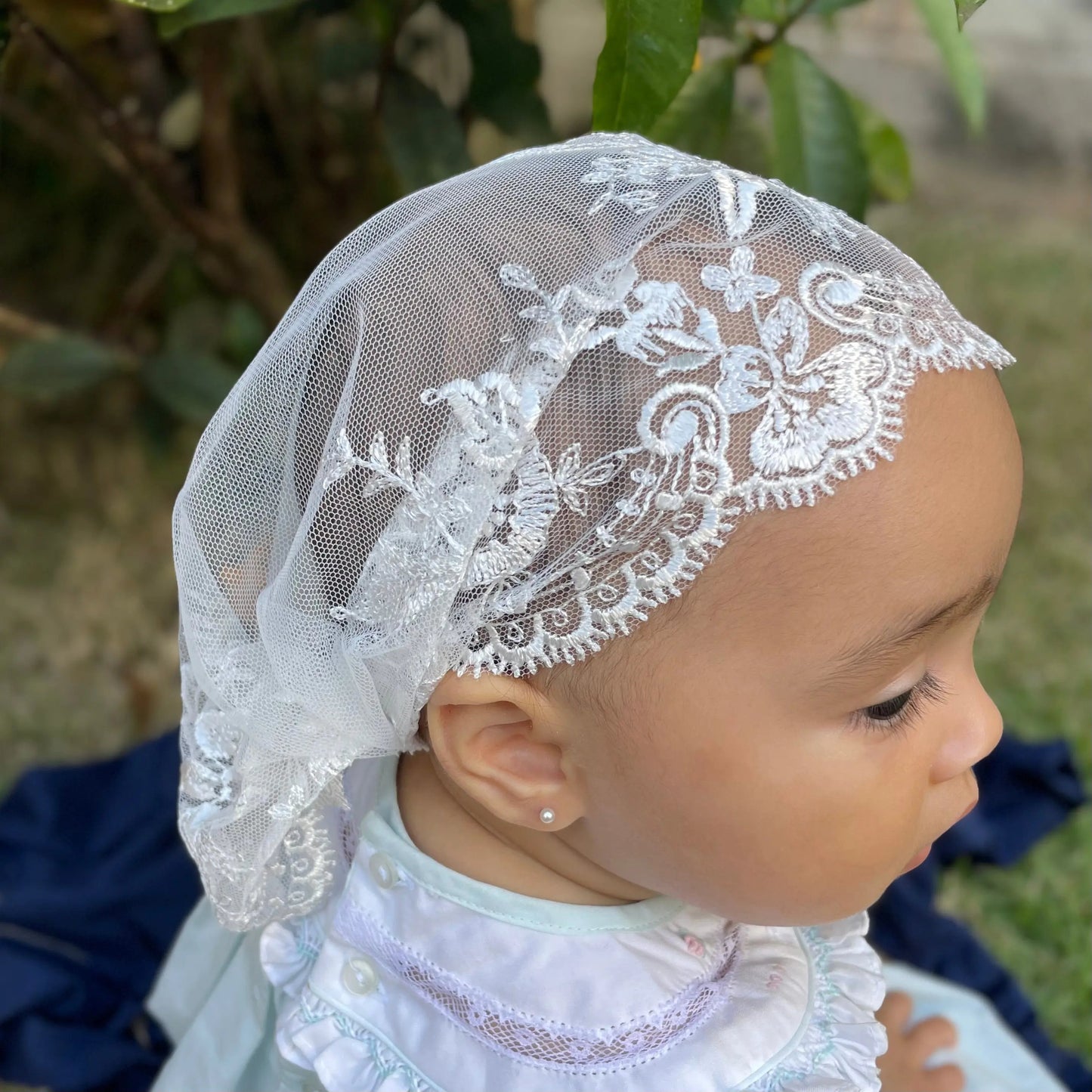 Top view of an infant wearing a white lace embroidered Catholic mass chapel veil.