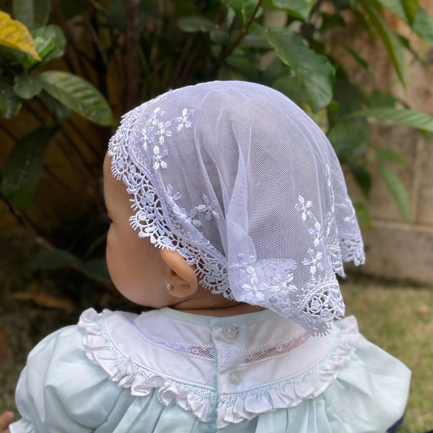Baby wearing a white embroidered lace traditional catholic mass veil headband.