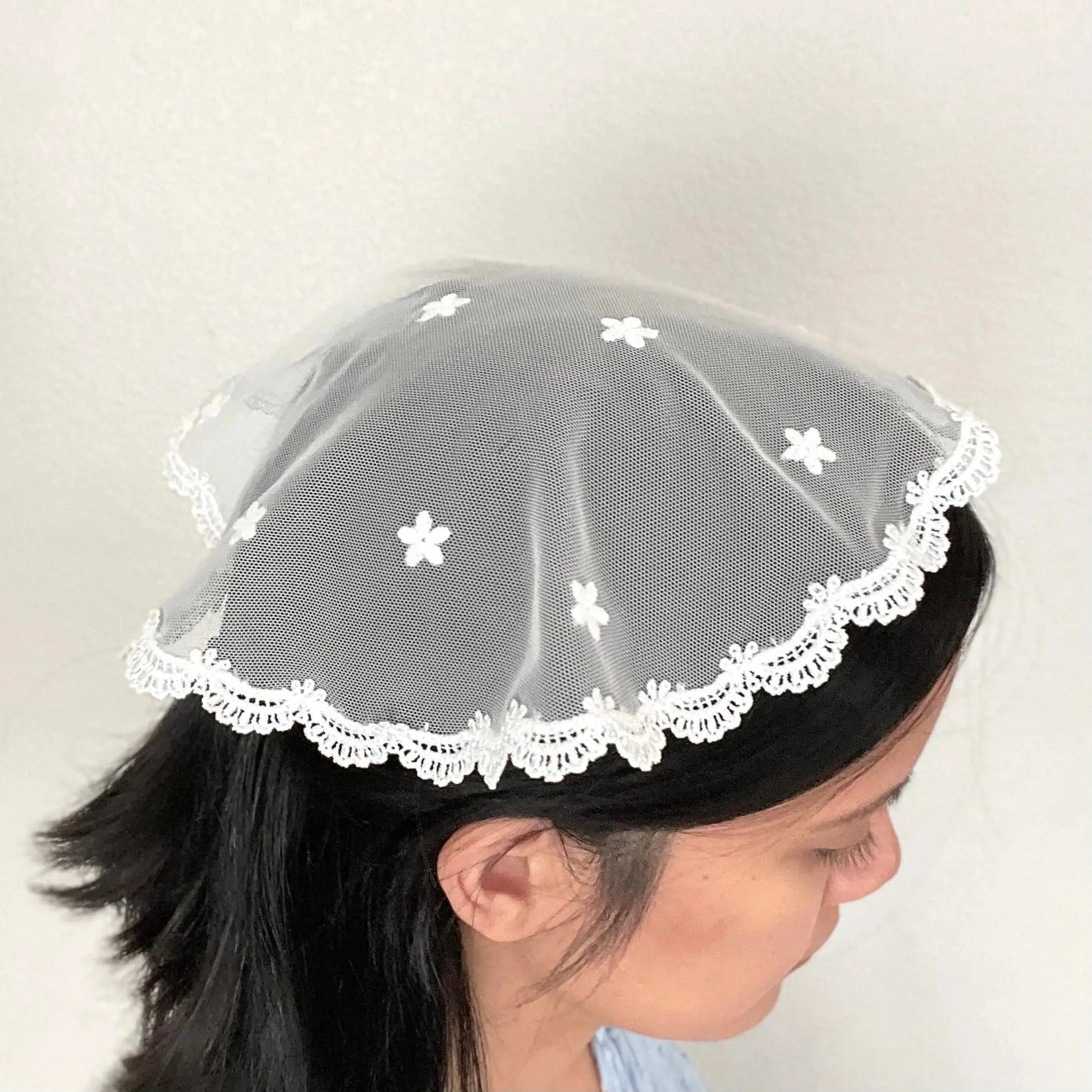 Girl in a traditional ivory circular cap veil with embroidered floral lace. 