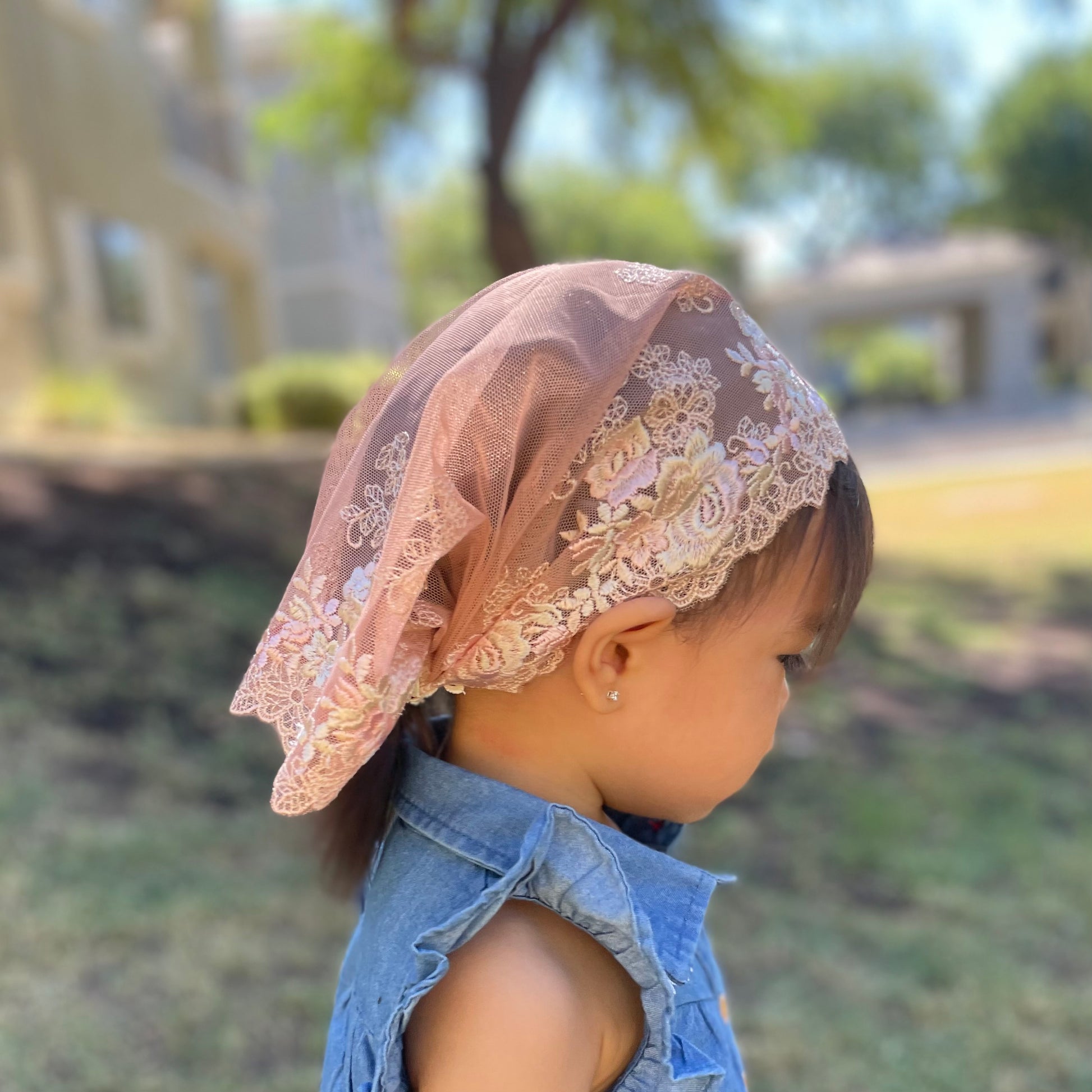 Baby wearing peach lace veil with rose embroidery. The toddler mantilla is perfect for Traditional Catholic Christian Mass