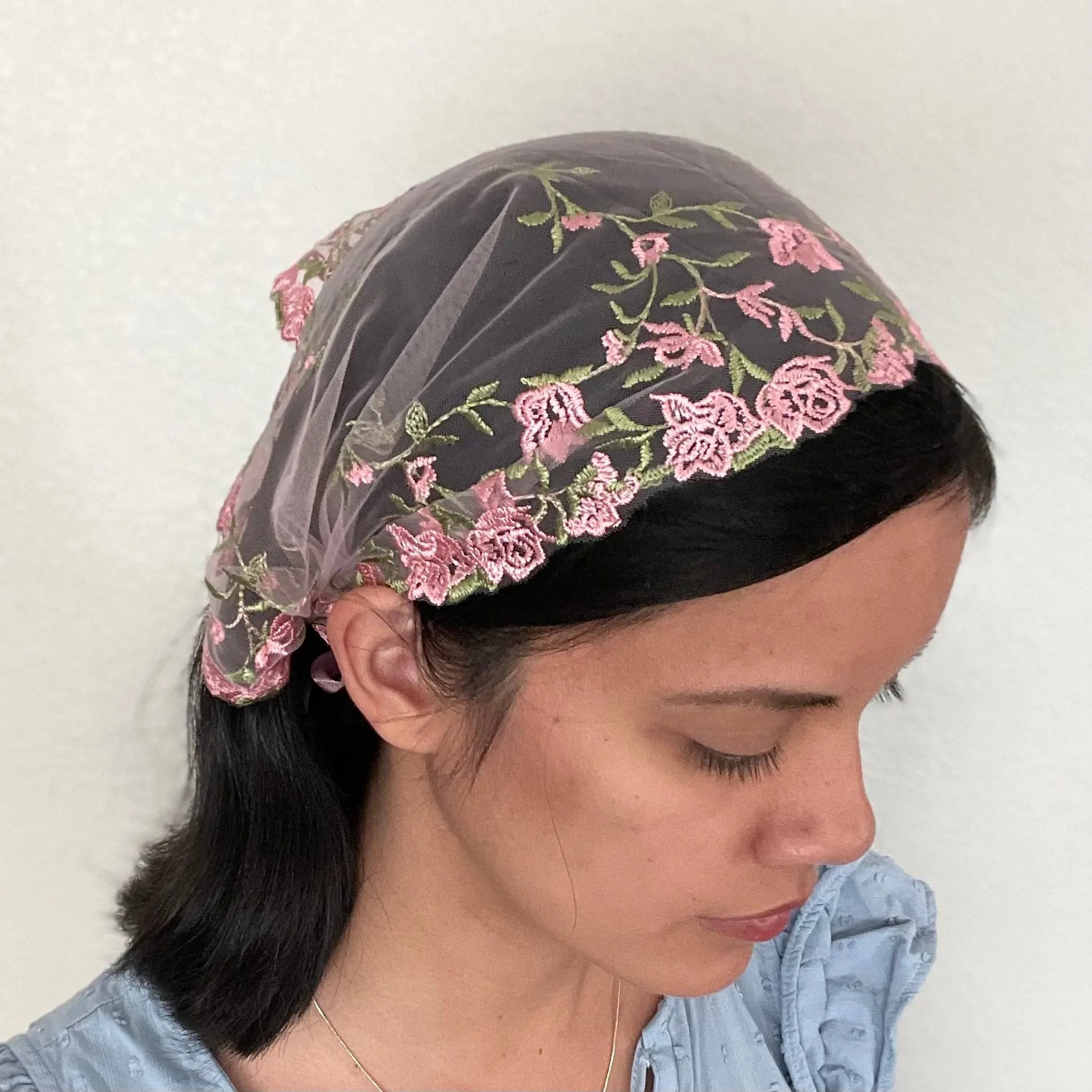 Girl wearing a pink lace chapel veil with rose embroidery. The small Traditional Catholic Christian Mass mantilla has ties