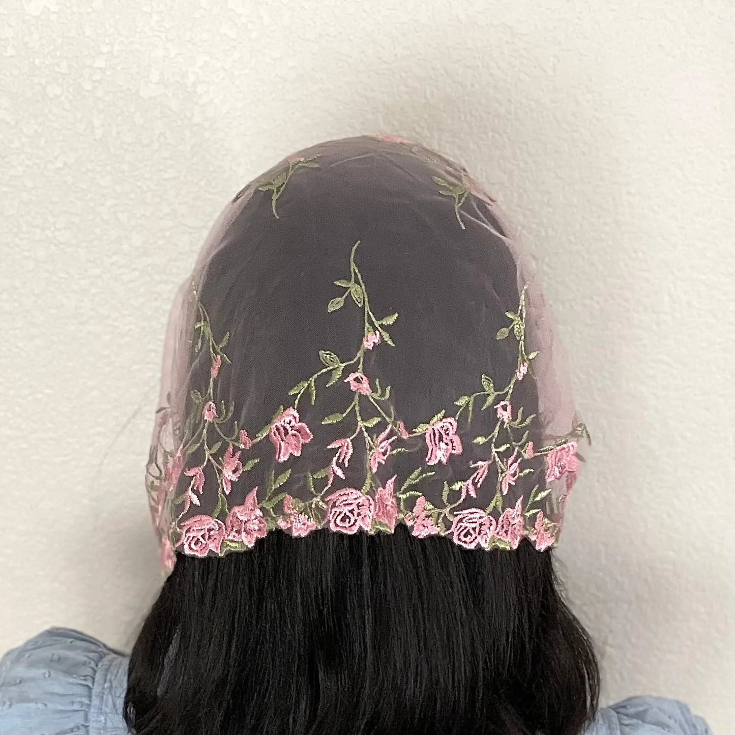 Woman wearing a pink lace chapel veil with rose embroidery. The small Traditional Catholic Christian Mass mantilla has ties