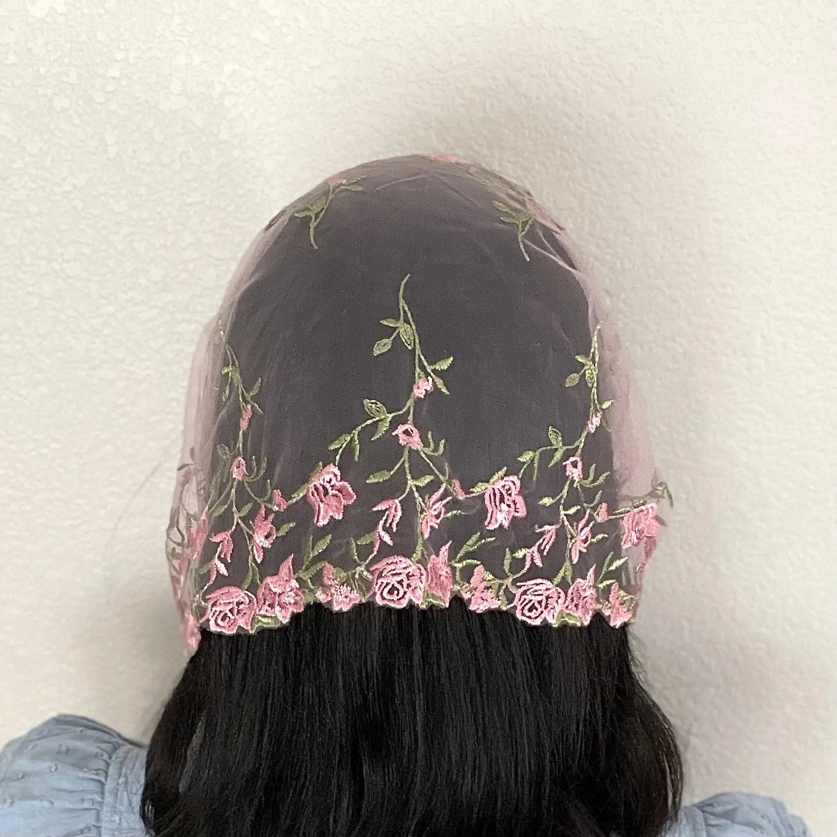 Woman wearing a pink lace chapel veil with rose embroidery. The small Traditional Catholic Christian Mass mantilla has ties