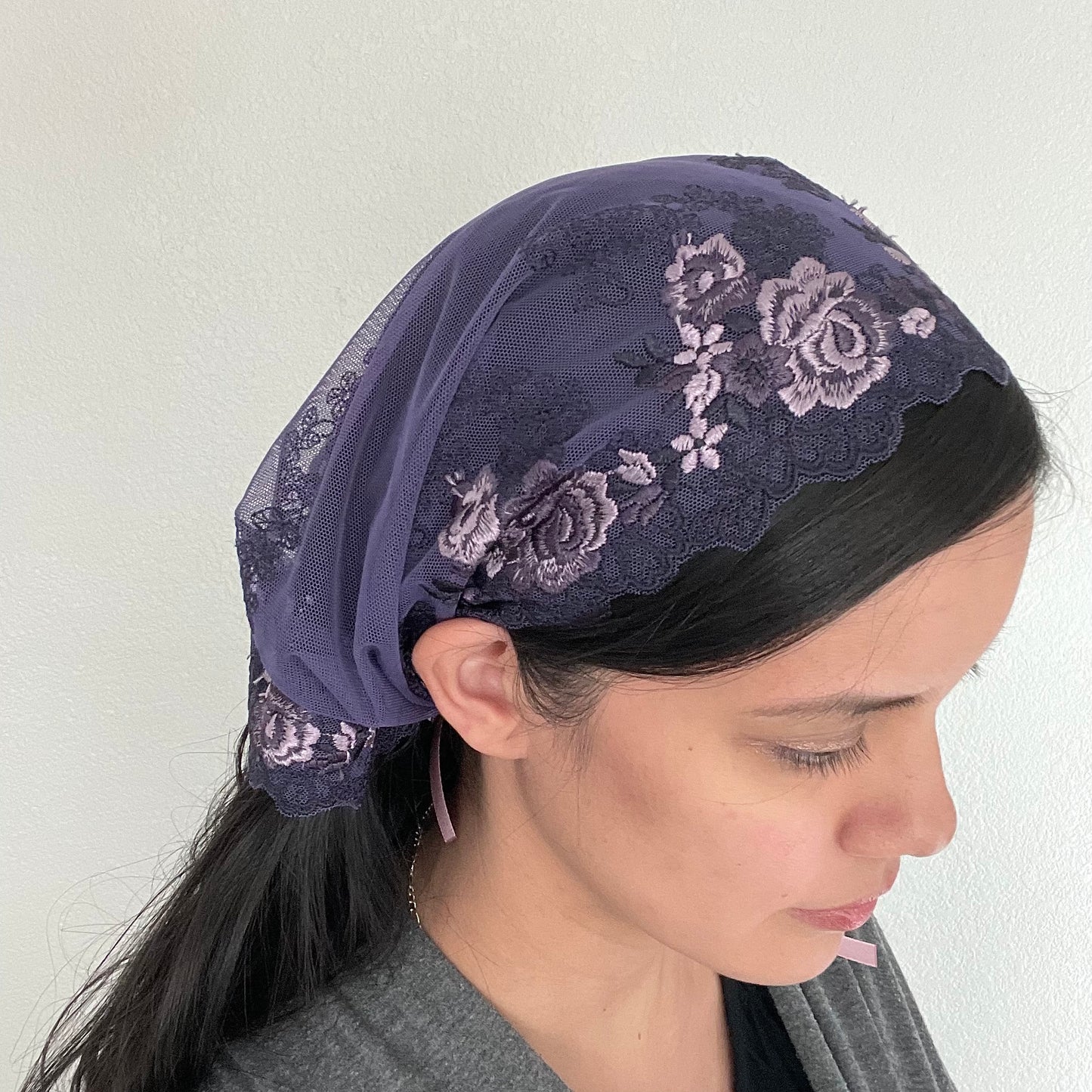 Woman wearing a dark purple lace chapel veil with rose embroidery. The Traditional Catholic Christian Mass mantilla has ties