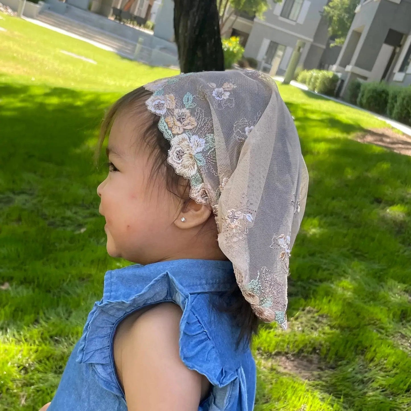 Infant wearing a beige colored lace embroidered Catholic mass chapel veil.