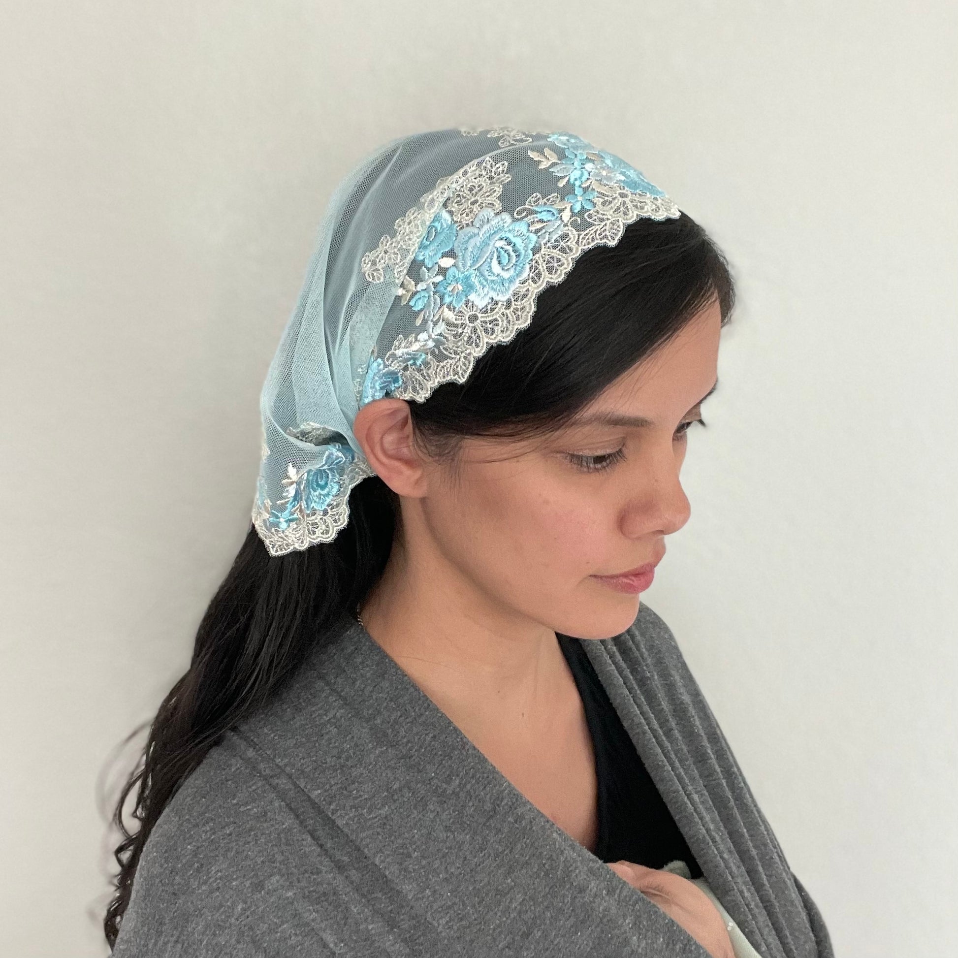 Girl wearing a blue lace chapel veil with rose embroidery. The small Traditional Catholic Christian Mass mantilla has ties