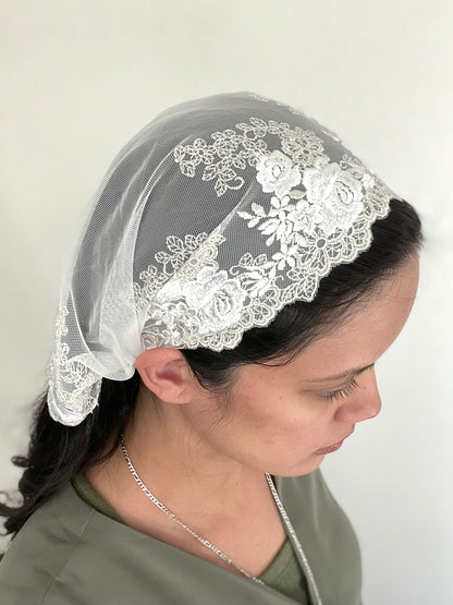 Girl wearing an ivory lace chapel veil with rose embroidery. The small Traditional Catholic Christian Mass mantilla has ties