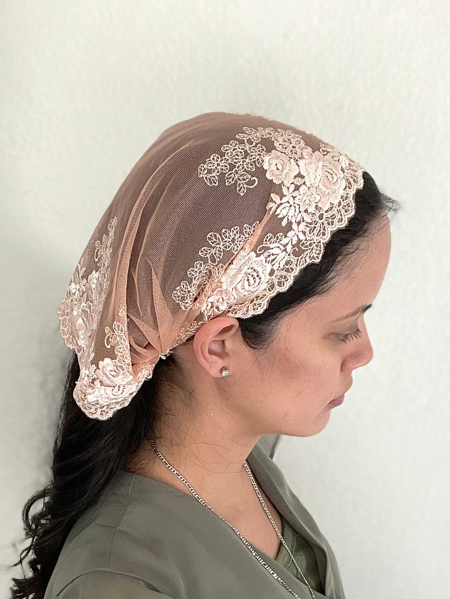 Girl wearing a peach lace chapel veil with rose embroidery. The small Traditional Catholic Christian Mass mantilla has ties