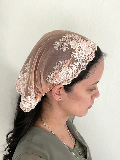 Girl wearing a peach lace chapel veil with rose embroidery. The small Traditional Catholic Christian Mass mantilla has ties