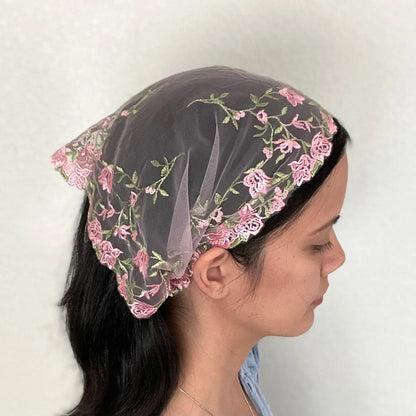 Girl wearing a lace chapel veil with pink rose embroidery. The small Traditional Catholic Christian Mass mantilla has ties