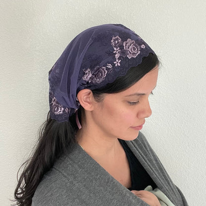 Girl wearing a purple lace chapel veil with rose embroidery. The small Traditional Catholic Christian Mass mantilla has ties