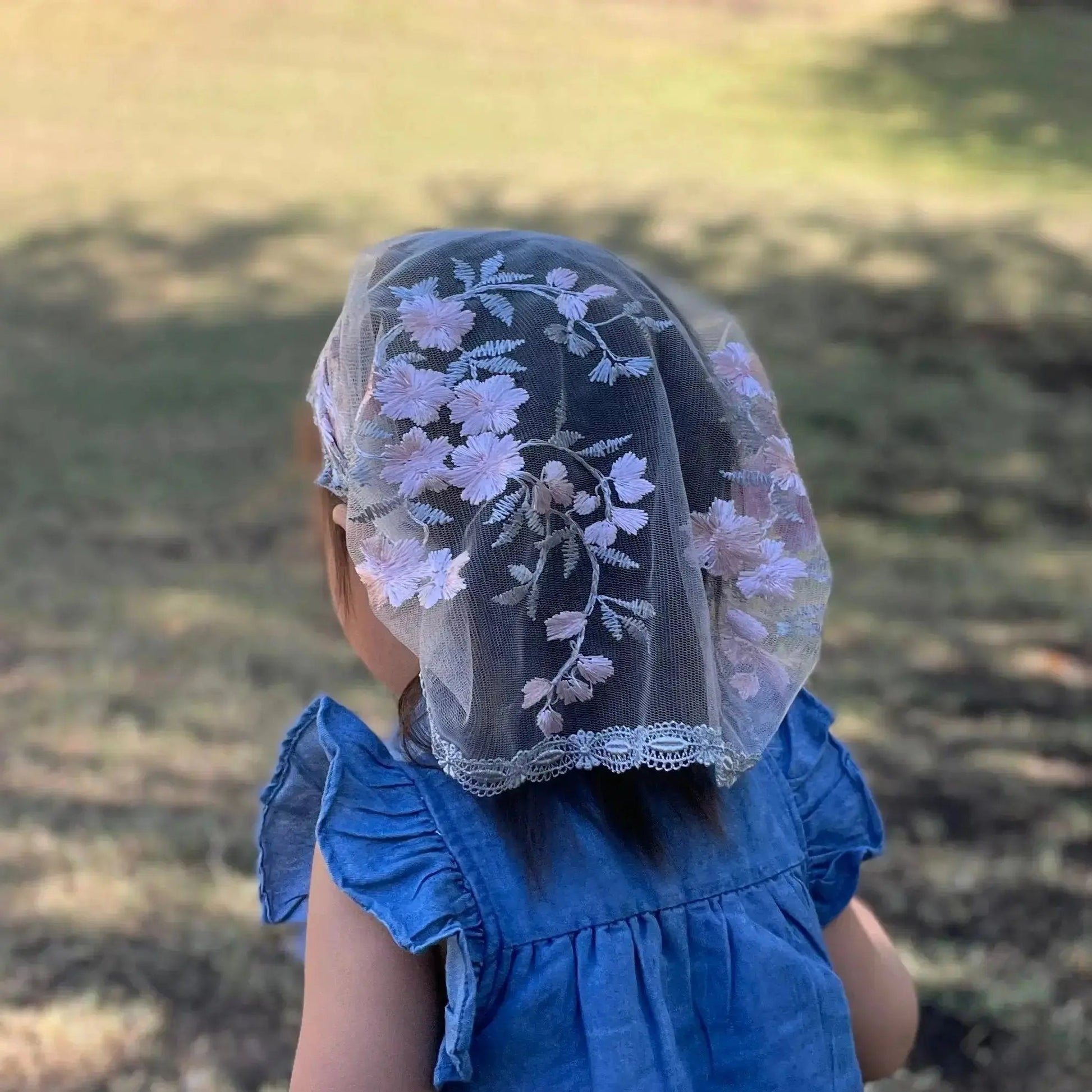Back view of a baby wearing a pink and grey colored Catholic Mass veil.