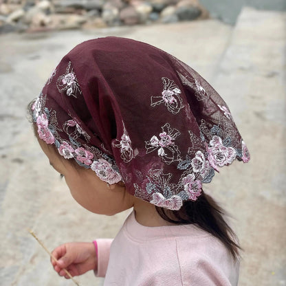 Toddler wearing a plum colored, finely embroidered lace traditional Christian chapel veil.