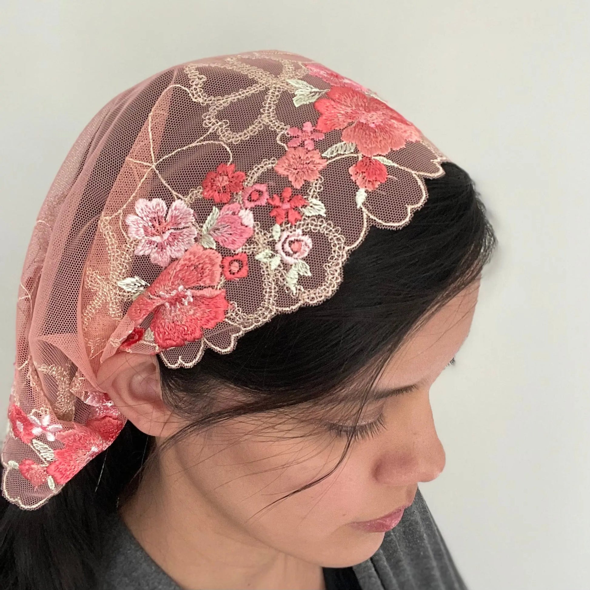 Woman wearing a pink floral embroidered lace chapel veil for Catholic Mass.