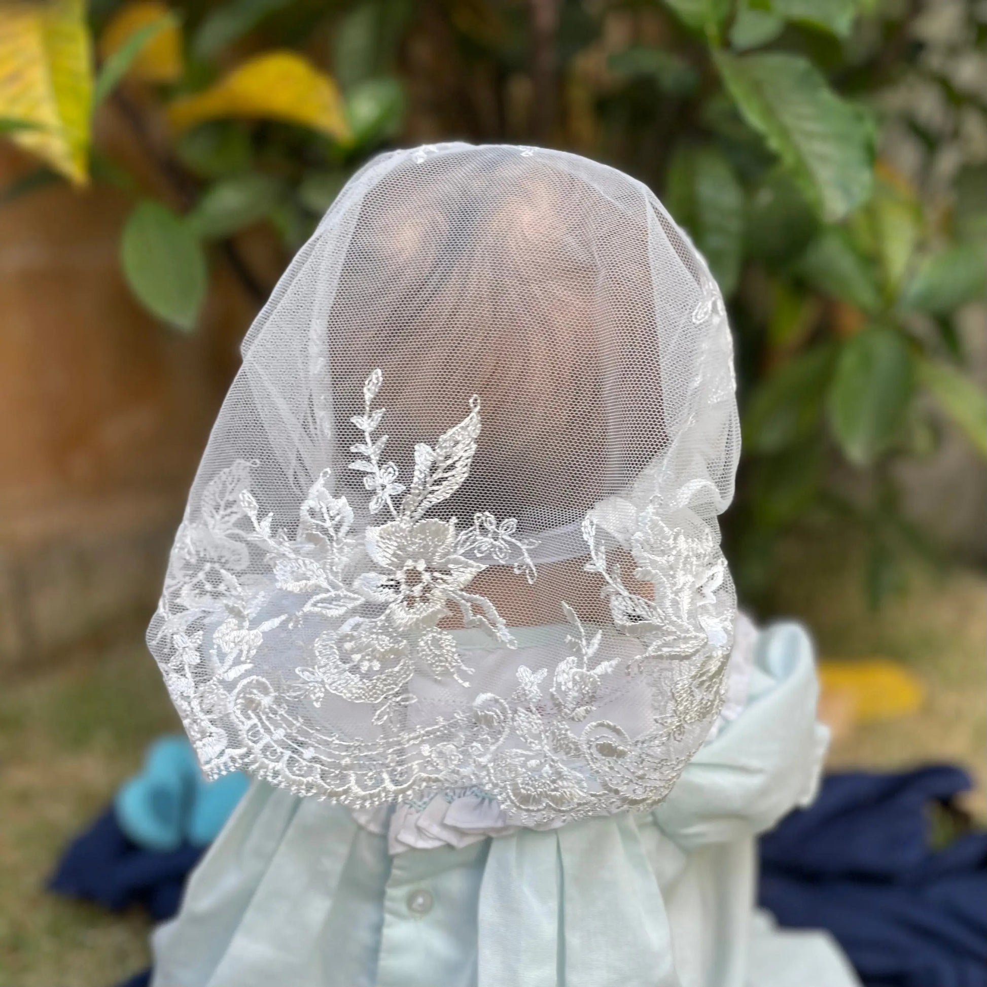 Infant wearing an ivory embroidered lace chapel veil for Traditional Catholic Mass.
