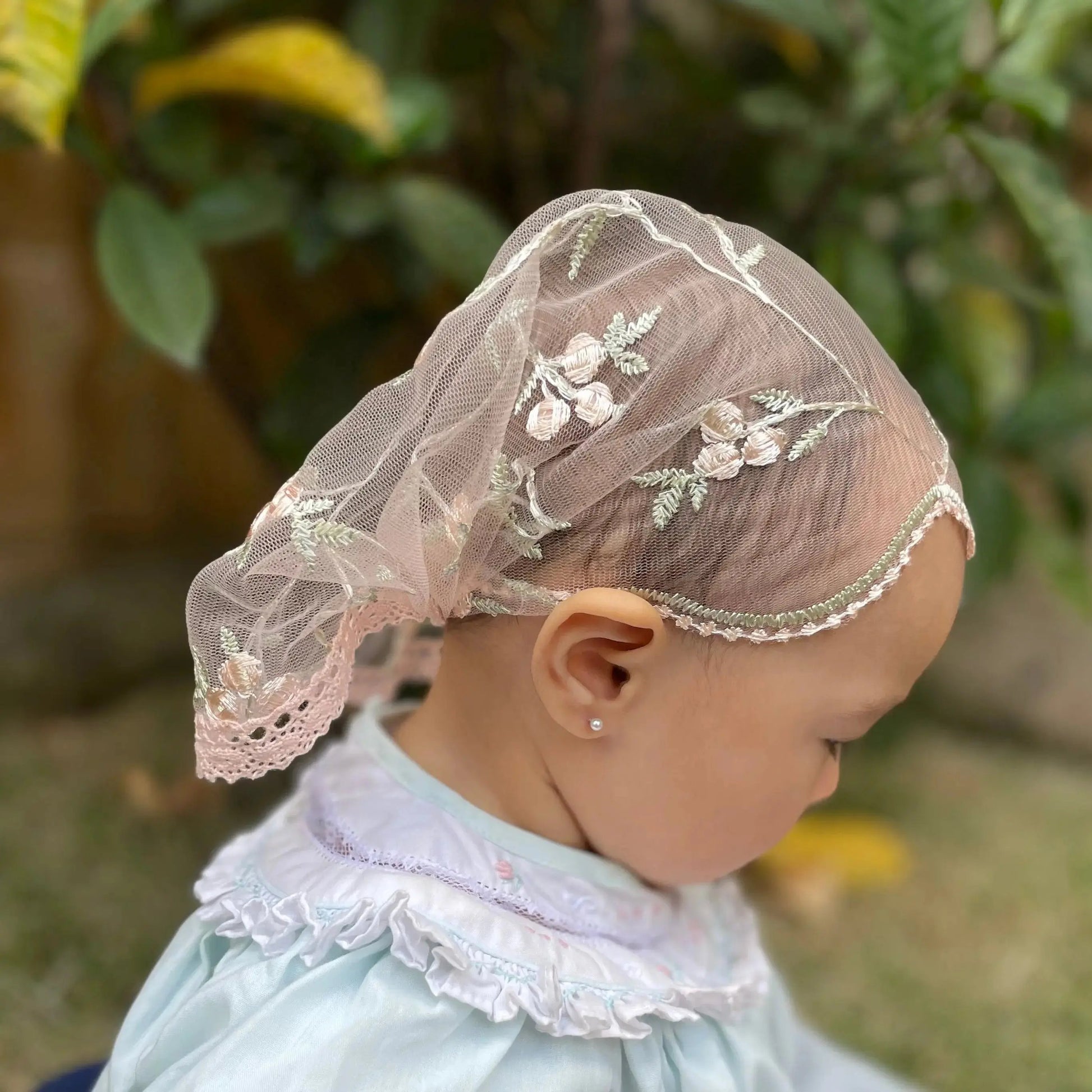 Baby wearing pink lace veil with embroidered little flowers. The mantilla is perfect for Traditional Catholic Christian Mass