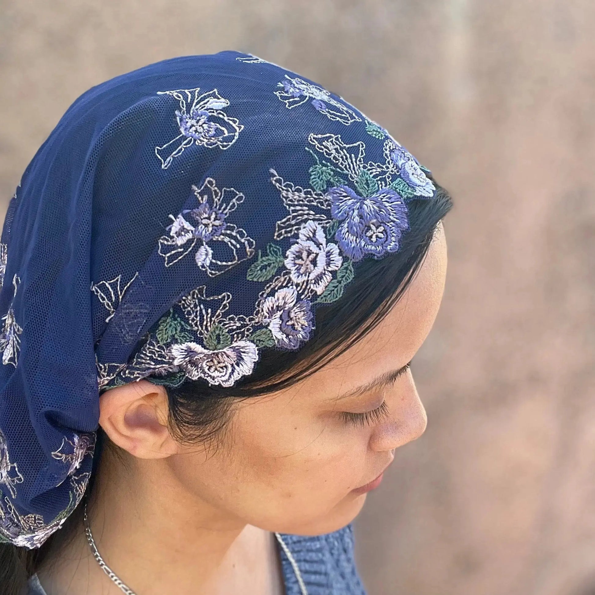 Girl wearing a dark blue lace embroidered traditional Catholic mass veil headscarf.