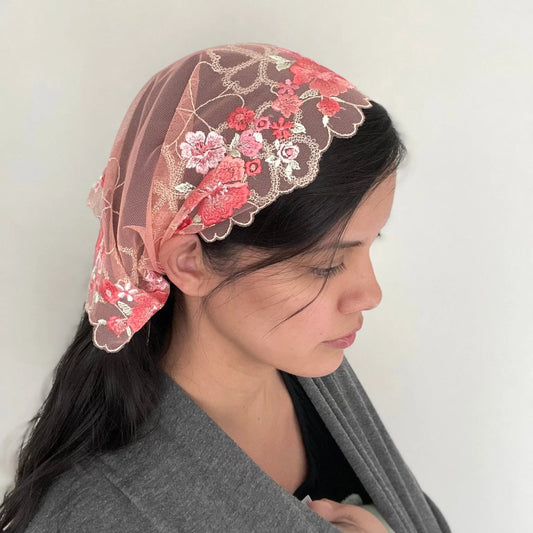 Girl wearing a pink lace embroidered traditional Christian mass veil headscarf.