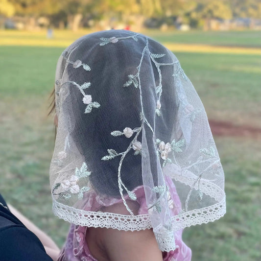 Infant wearing pale pink lace veil with floral embroidery. The mantilla is perfect for Traditional Catholic Christian Mass.
