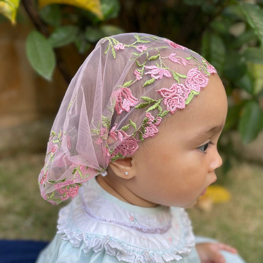 Infant wearing pink embroidered lace veil, a traditional Catholic chapel veil.
