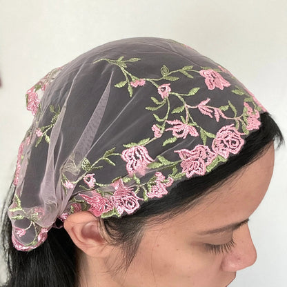 Girl wearing a small pink lace chapel veil with rose embroidery. The Traditional Catholic mantilla may be worn for Mass.