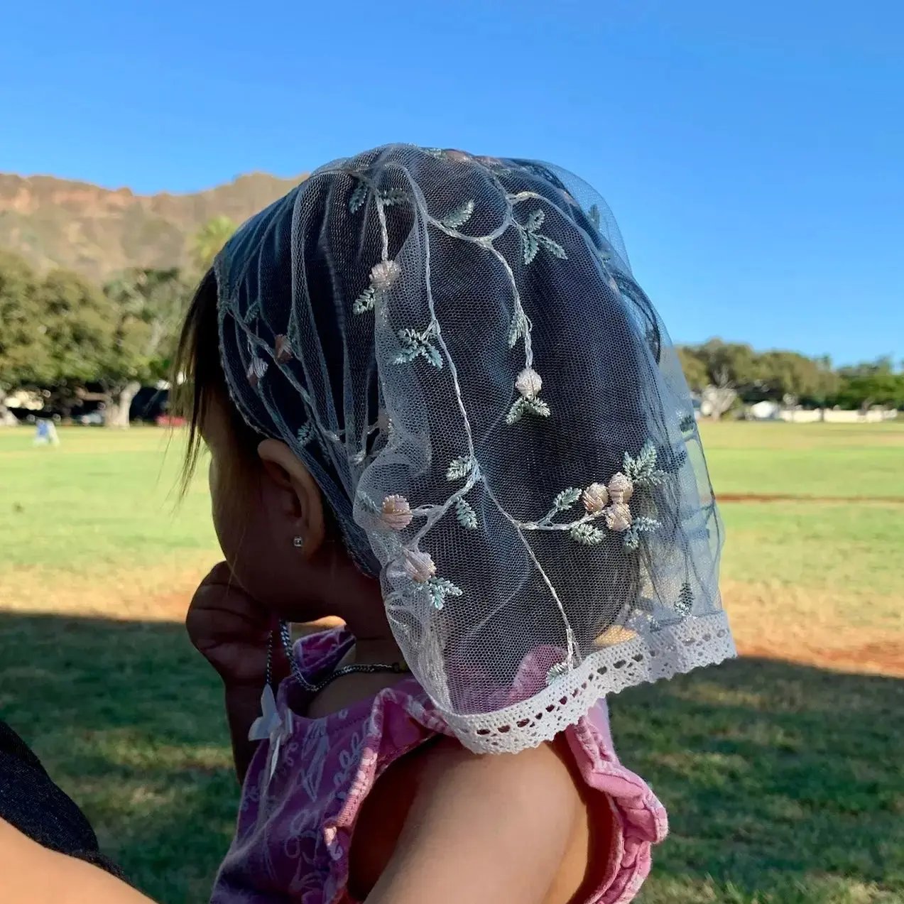 Infant wearing D shape pink lace veil with floral embroidery. The mantilla is perfect for Traditional Catholic Christian Mass