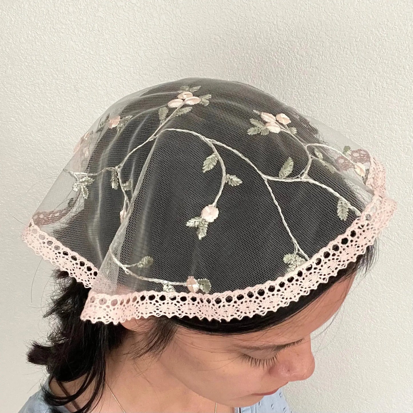 Girl wearing a pale pink floral embroidered lace cap chapel veil for Catholic mass.