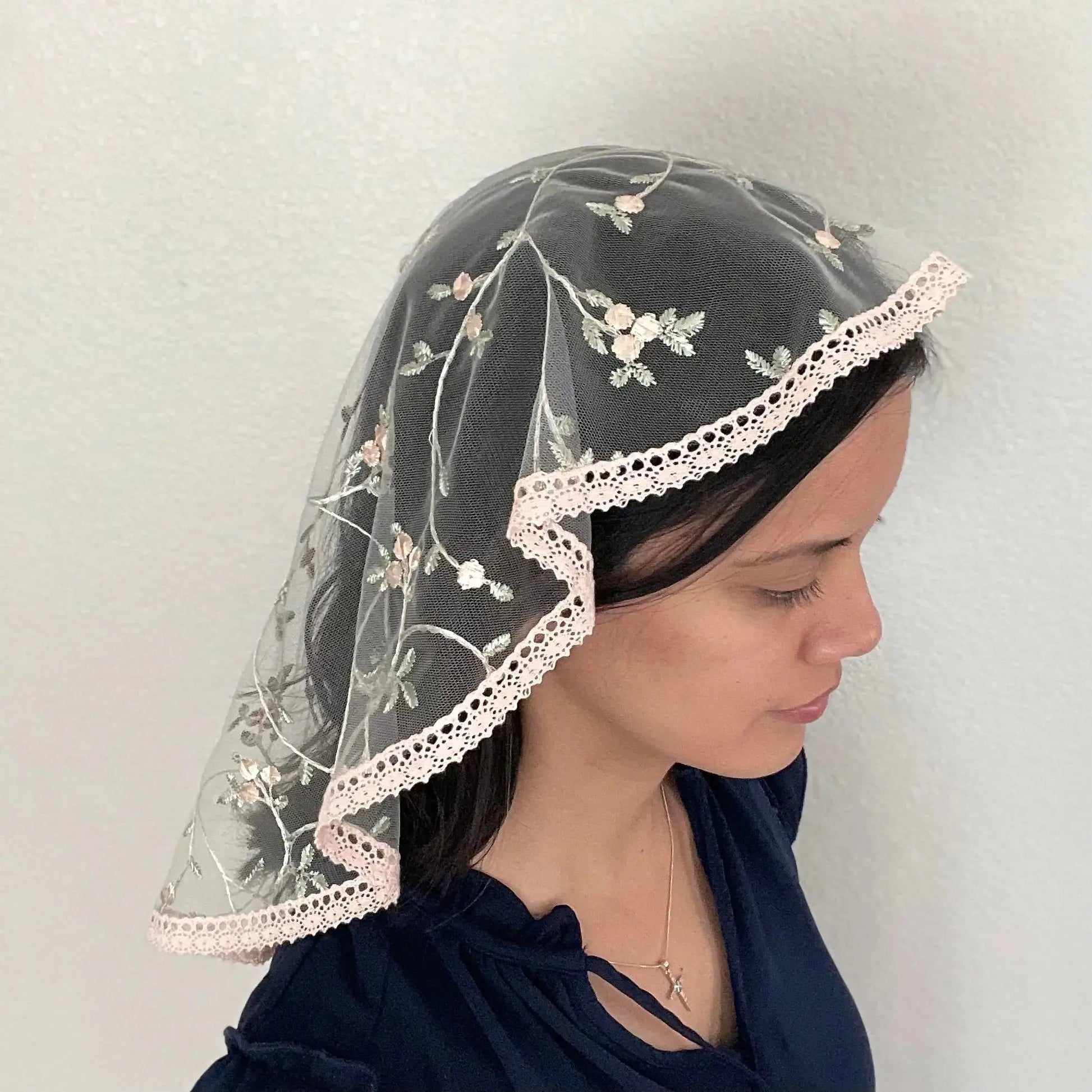 Girl wearing a pink floral embroidered lace oval veil for Catholic mass.