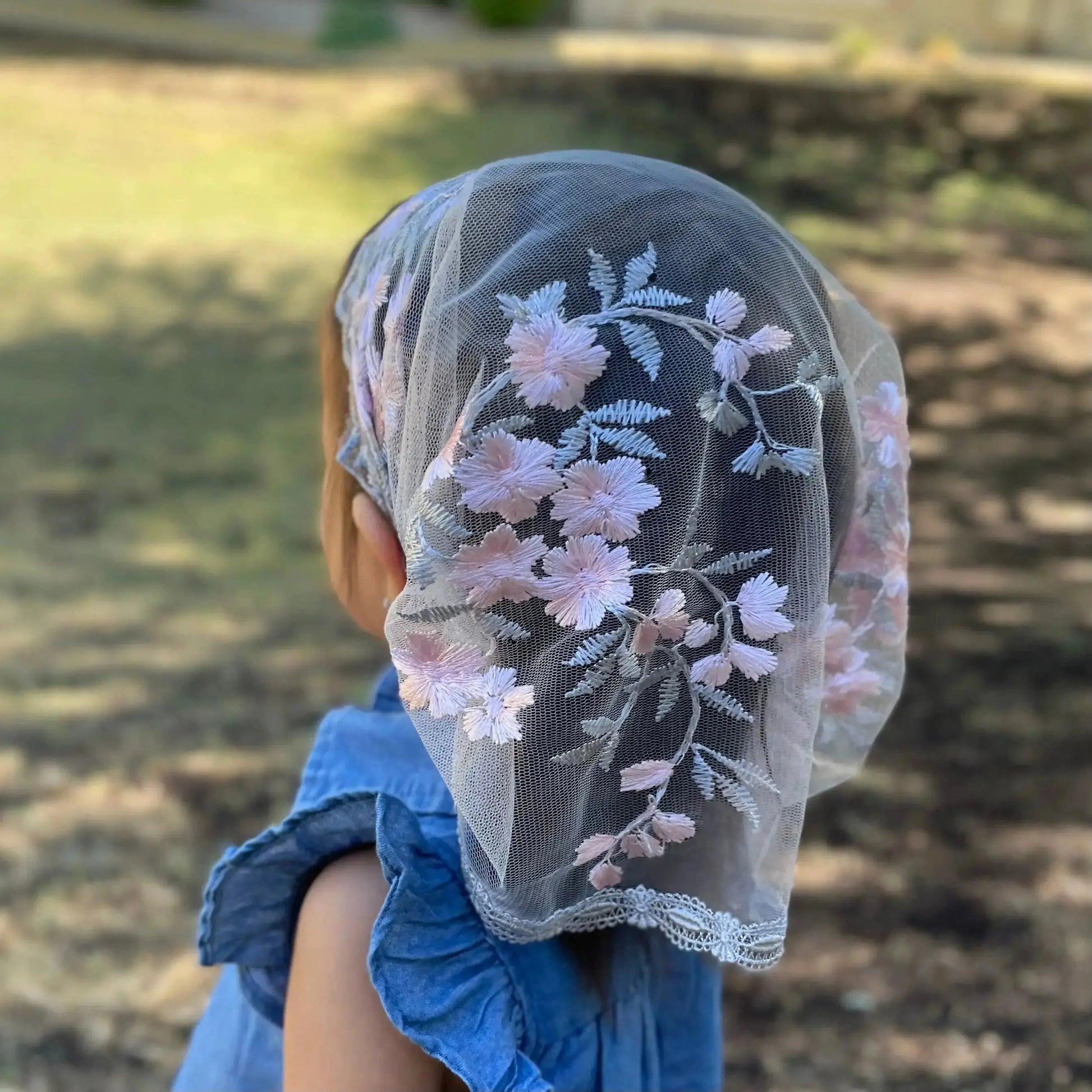Back view of a toddler wearing a pink and grey lace Catholic mantilla.