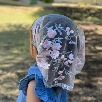 Back view of a toddler wearing a pink and grey lace Catholic mantilla.