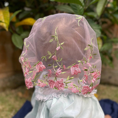 Back view of an infant wearing a pink roses embroidered lace chapel veil for Catholic mass. 
