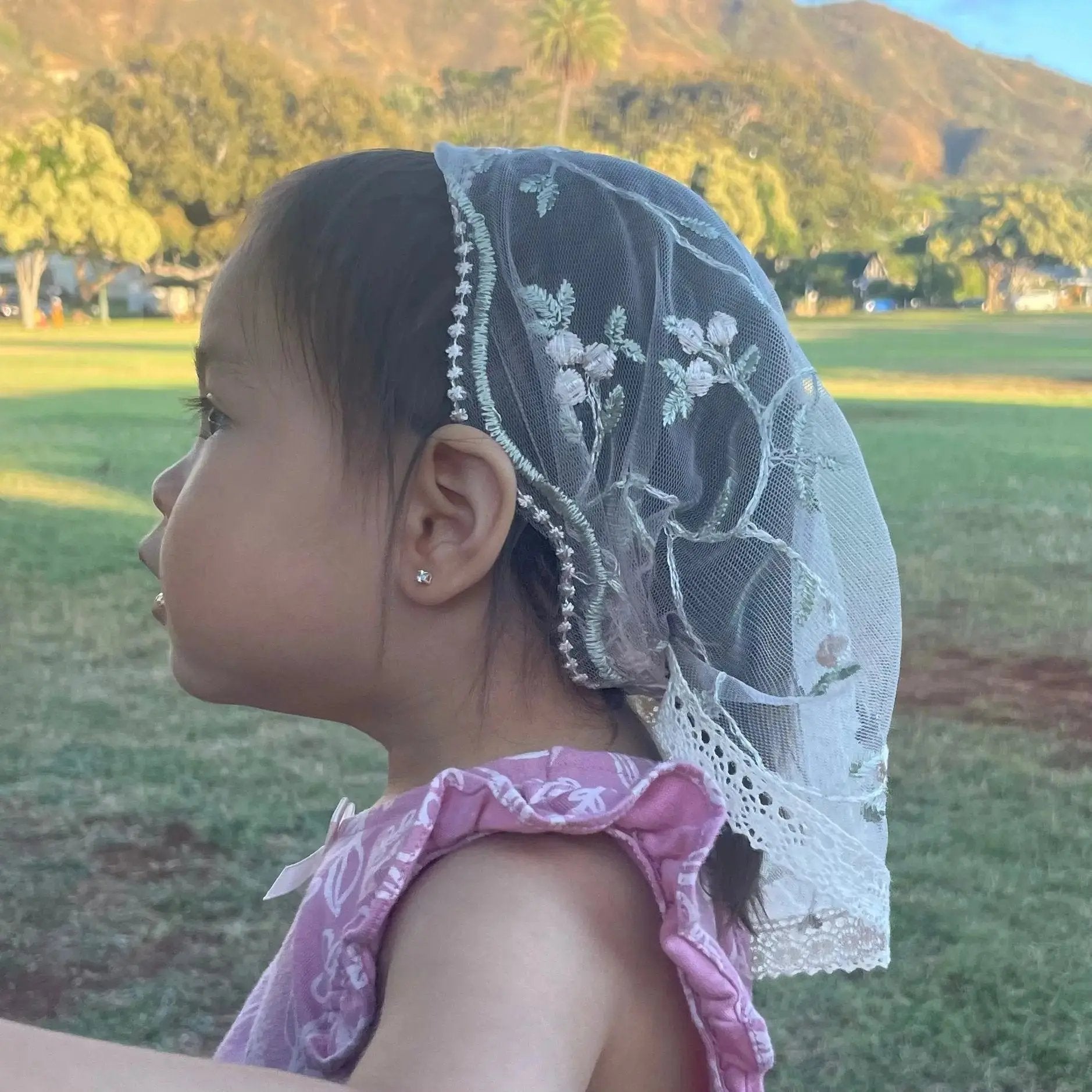 Baby wearing pale pink lace veil with floral embroidery. The mantilla is perfect for Traditional Catholic Christian Mass.