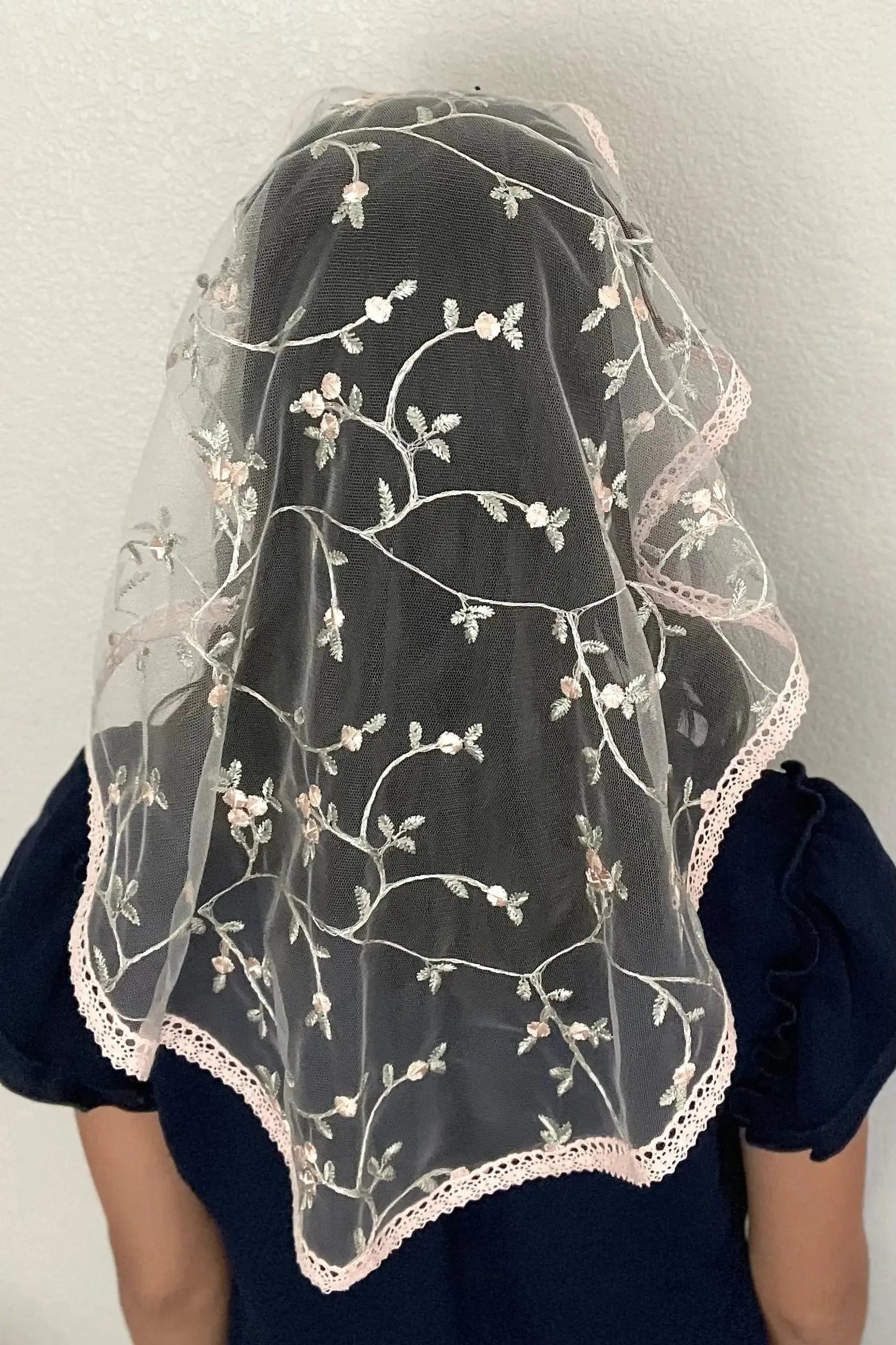 Back view of girl wearing a floral pink embroidered lace oval veil for Catholic mass.
