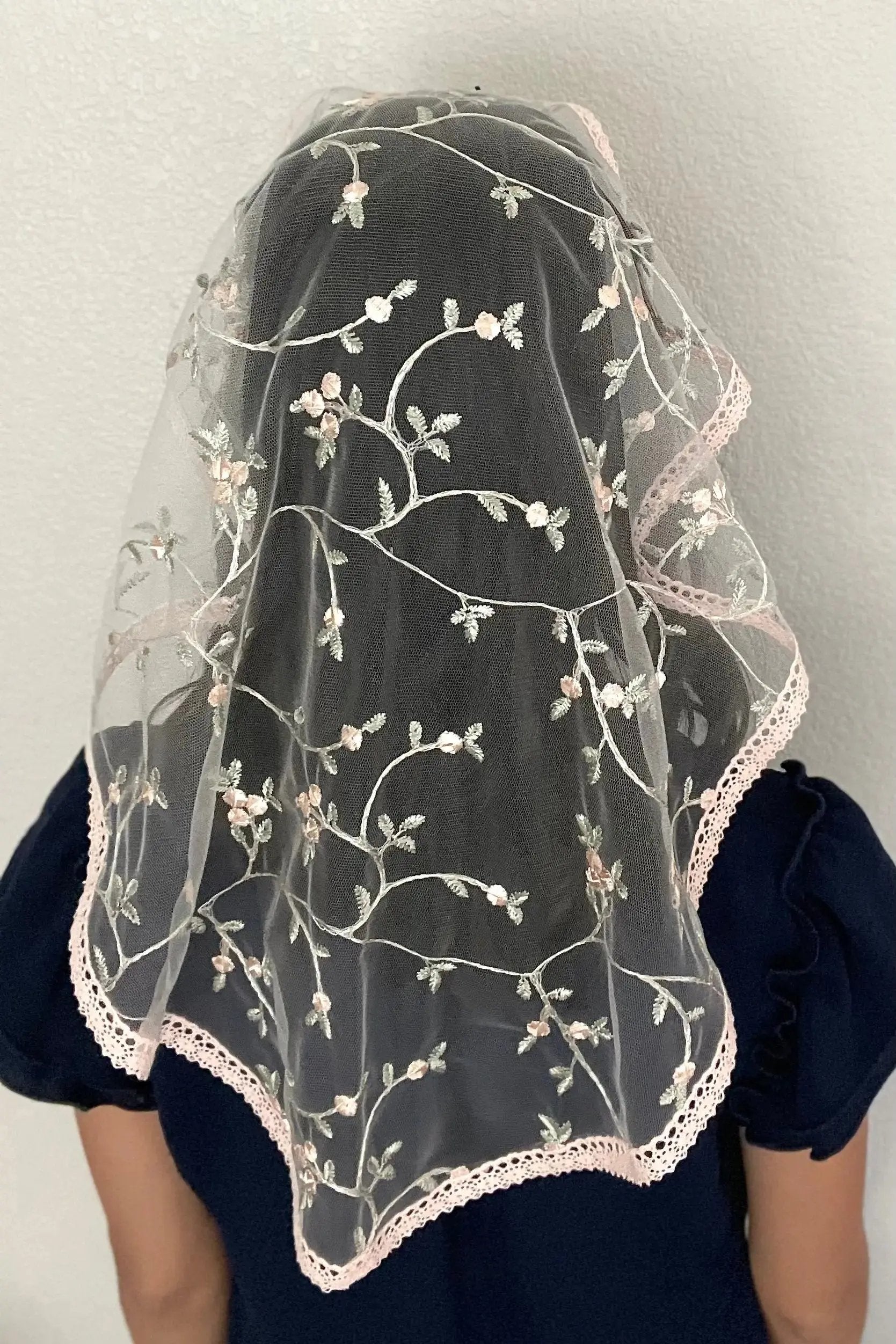 Back view of girl wearing a floral pink embroidered lace oval veil for Catholic mass.