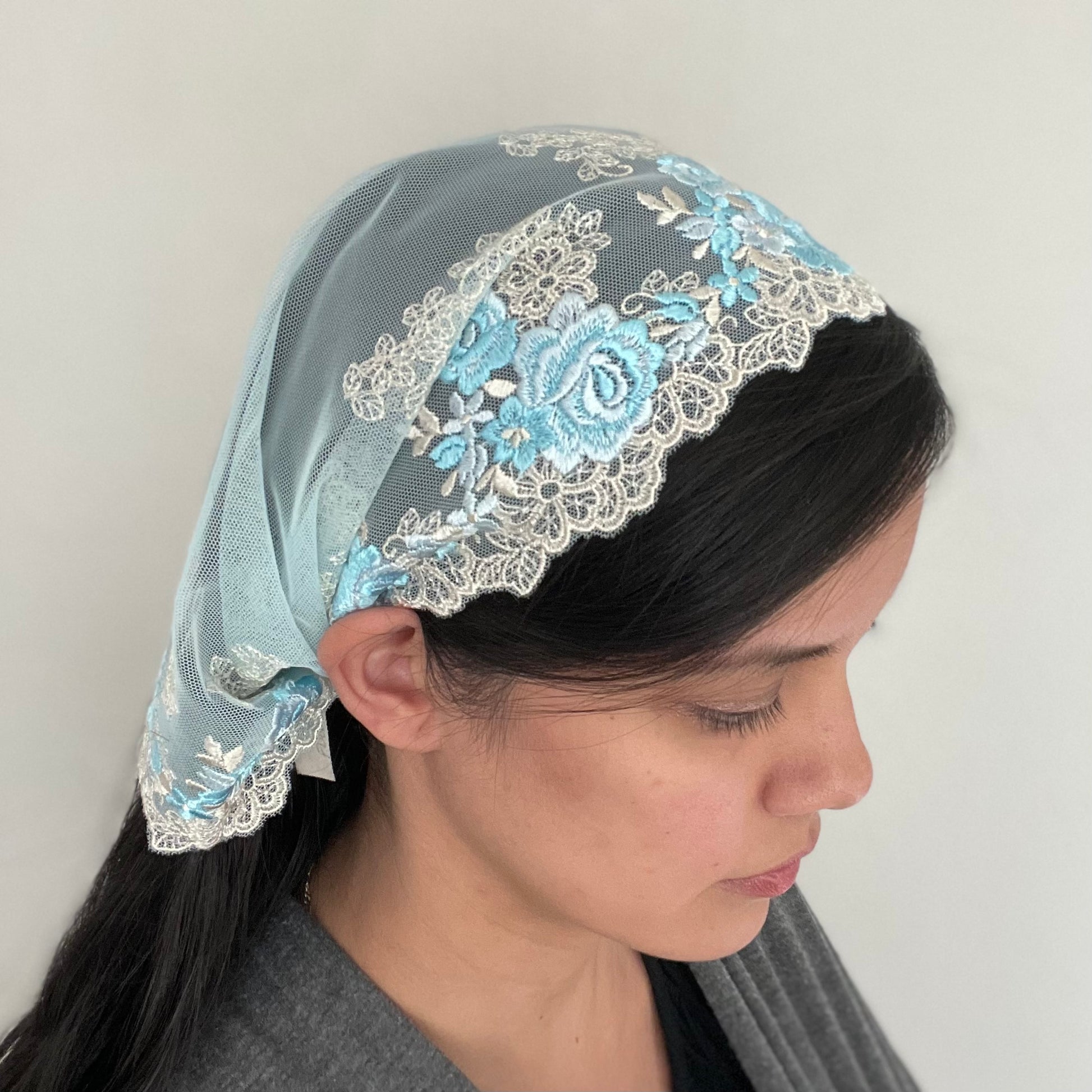 Girl wearing a light blue chapel veil with rose embroidery. The small Traditional Catholic Christian Mass mantilla has ties