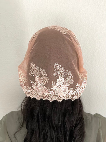 Girl wearing a lace chapel veil with peach rose embroidery. The small Traditional Catholic Christian Mass mantilla has ties